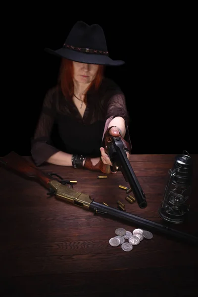 Дика західна дівчина стріляє з револьверної гармати на столі з боєприпасами і срібними монетами — стокове фото