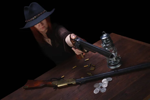 Wild west girl shooting from revolver gun at the table with ammunition and silver coins — ストック写真