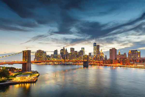 New York, New York, USA downtown Manhattan city skyline over the East River with the Brooklyn Bridge at dusk.