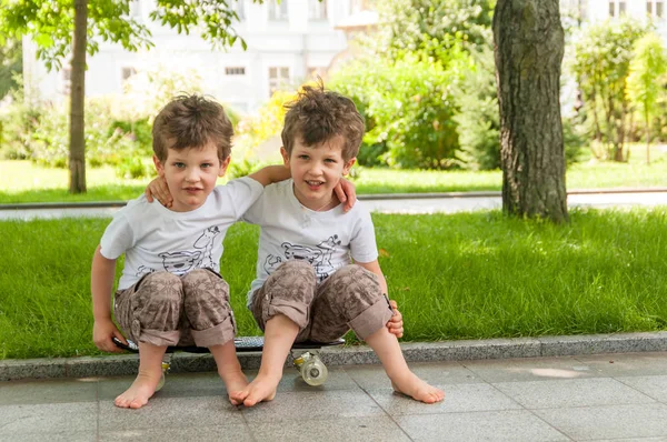 Tweeling jongens omarmd zittend op het skateboard buiten in park — Stockfoto