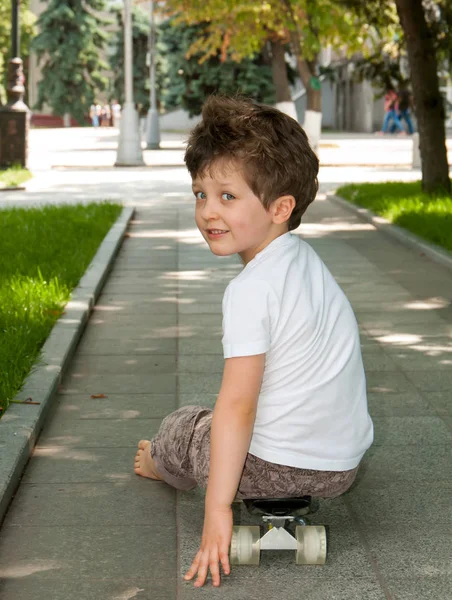 El chico está sentado en el monopatín en el parque — Foto de Stock