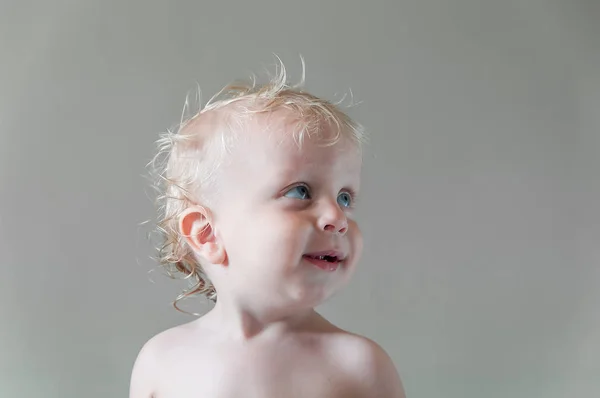 Blauw-eyed blond kind glimlachen kijkt weg op een grijze achtergrond — Stockfoto