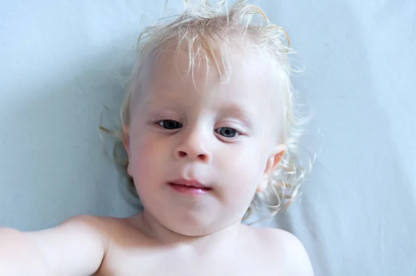 Blauw-eyed blond baby ligt op een blauwe achtergrond — Stockfoto
