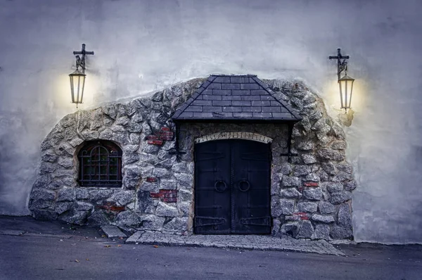 Puerta de hierro de estilo antiguo en una pared de piedra, dos linternas viejas en el wal — Foto de Stock
