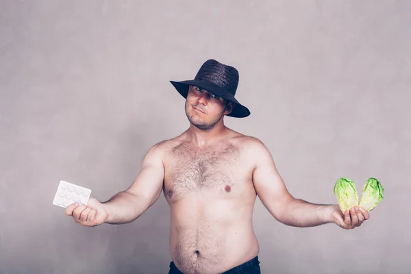 Naked corpulent man giving pharmaceuticals and vegetable — Stock fotografie