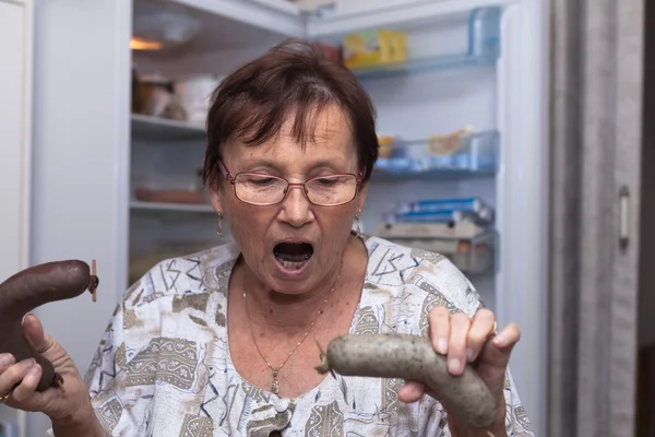 Geschokt Senior vrouw houden varkensvlees leverworst — Stockfoto