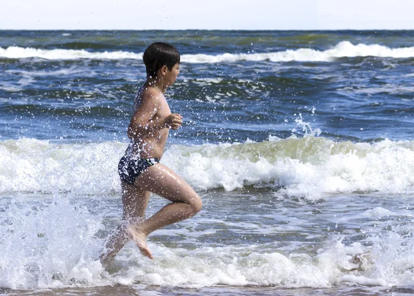 Šťastný malý chlapec běží s splash na moři. — Stock fotografie