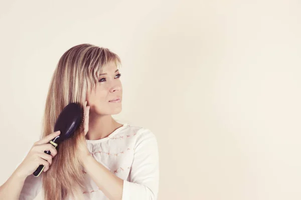 Portrait of beautiful young woman combing her hair and smiling — Stock Photo, Image