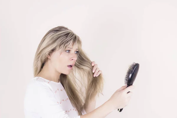 Perda de cabelo. Deprimida jovem mulher olhando para sua escova de cabelo e expressando negatividade — Fotografia de Stock