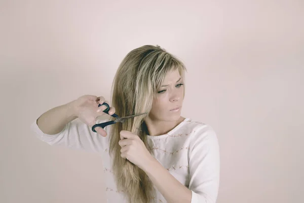Angry blonde woman cuts her hair with scissors — Stock Photo, Image