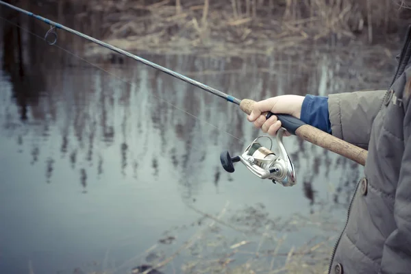 Woman hand with spinning and reel on the riverbank — Stock Photo, Image