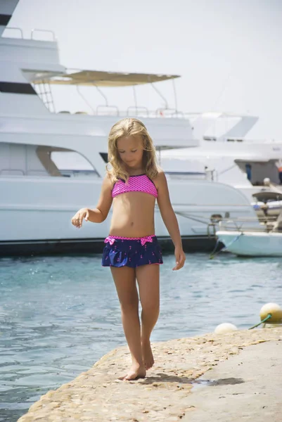 Красивая девушка прогуливается по берегу камня на фоне яхт — стоковое фото