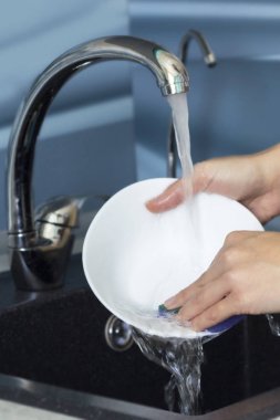 Kadın elleri lavaboda akan suyun altında bulaşıkları yıkıyor..