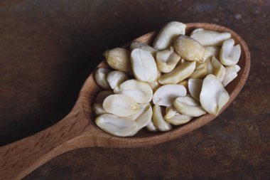 Paslı bir arka plan üzerine bir tahta kaşık içinde kavrulmuş fıstık soyulmuş.