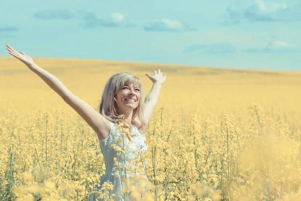 Женщина с длинными волосами стоит на желтом лугу рапса с поднятыми руками. Понятие свободы и счастья . — стоковое фото