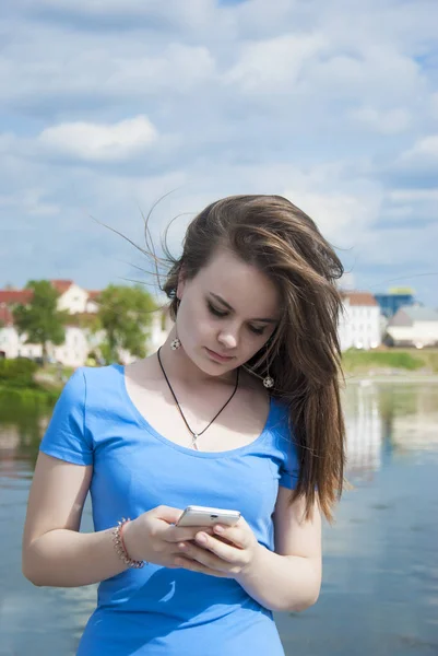 Menina adolescente bonita fica em um fundo da cidade com um telefone celular envia uma mensagem . — Fotografia de Stock