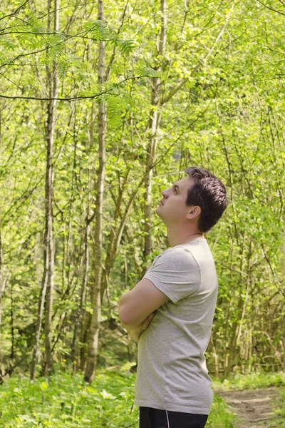 Thoughtful young man with crossed arms standing in the forest on sunny spring day. — Stock Photo, Image