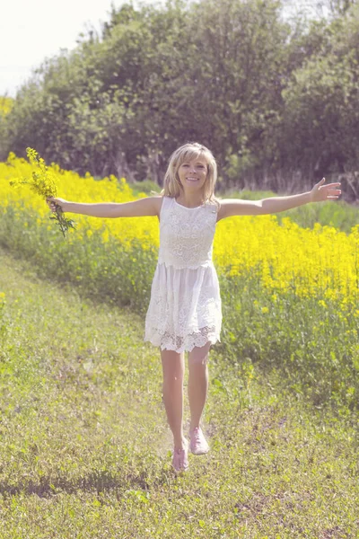 Fille avec bouquet de fleurs de viol marchant sur la route de campagne . — Photo