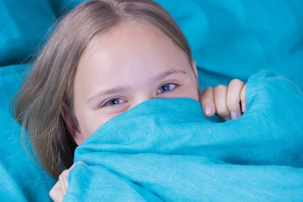 Schönes junges Mädchen im Bett liegend und schlafend. Teenie-Mädchen mit offenen Augen bedeckt morgens ihr Gesicht mit einer blauen Decke. zu wenig Schlaf Konzept zu bekommen. Kopierraum. — Stockfoto