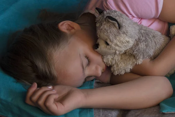 Kleines blondes Kind schläft in seinem Bett mit Spielzeug. — Stockfoto