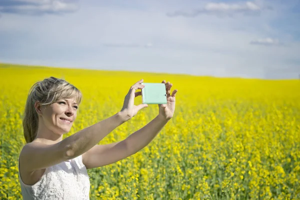 技術、夏の休日、休暇と人々 の概念 - 菜の花畑のスマート フォンによる womantaking selfie の手. — ストック写真