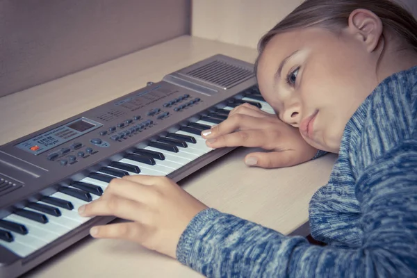 Девочка устала от обучения играть на синтезаторе и грустной лжи на столе . — стоковое фото