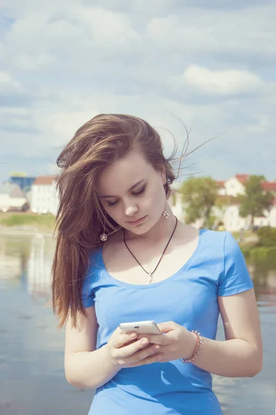 Menina adolescente bonita fica em um fundo da cidade com um telefone celular envia uma mensagem . — Fotografia de Stock