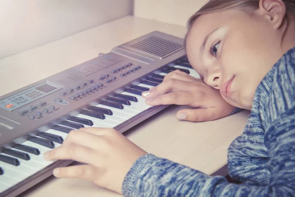 Девочка устала от обучения играть на синтезаторе и грустной лжи на столе . — стоковое фото