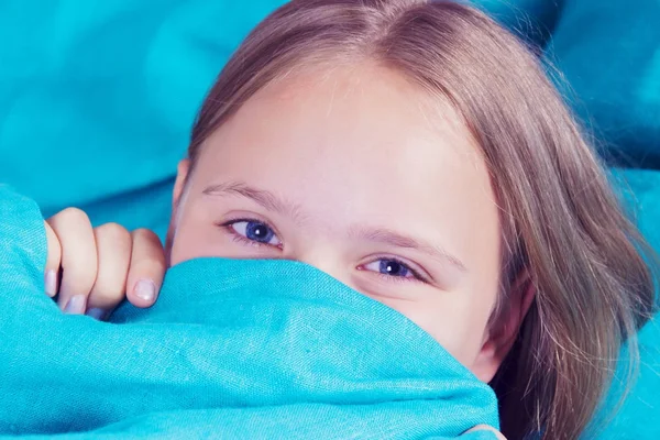 Menina bonita deitada na cama e dormindo. Menina adolescente com olhos abertos cobre o rosto com cobertor azul pela manhã. Não tenha suficiente conceito de sono. Espaço de cópia . — Fotografia de Stock