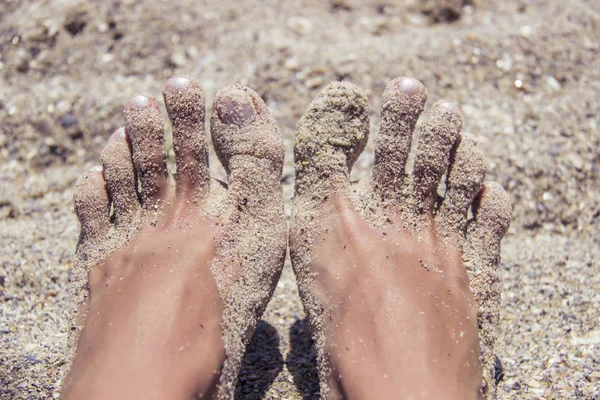 Pies desnudos de mujer cubiertos de arena en la playa . — Foto de Stock