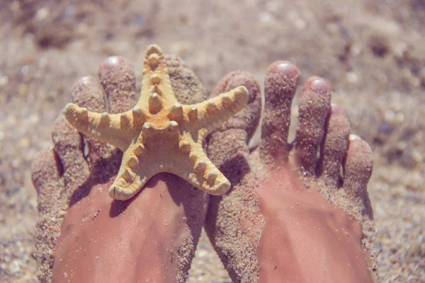Mulher relaxante na praia com pés arenosos e estrelas do mar . — Fotografia de Stock