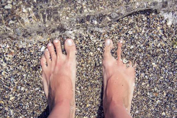 Pies desnudos de mujer cubiertos de arena en la playa . — Foto de Stock