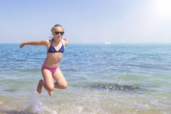 少女在蓝色的大海岸边沙滩上跳跃在暑假期间在白天的时间. — 图库照片