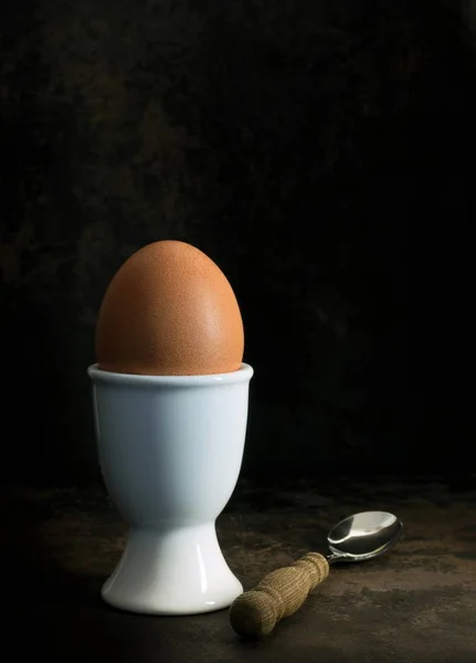 A low light image of a boiled egg in a cup on a dark background with copy space for your text