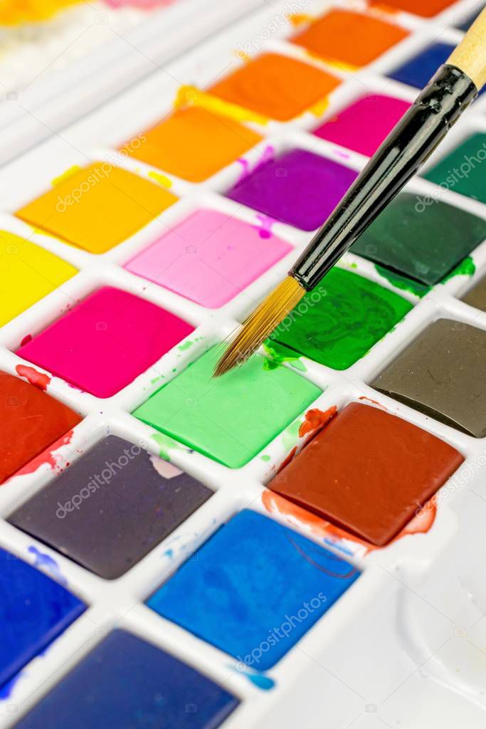 An artists paint brush and a box of colourful water colour paints