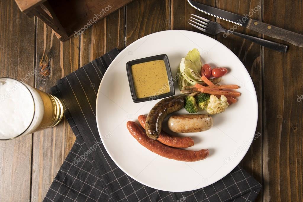 beer and delicious grilled sausages on wooden table, top view