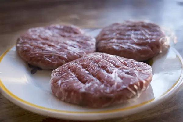 Hambúrguer de carne congelada embrulhado em filme plástico — Fotografia de Stock