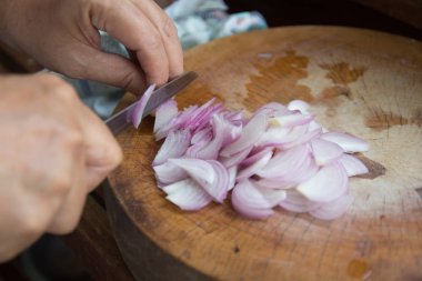 Kadın, mutfaktaki eski ahşap kesim tahtasına mor soğan dilimledi. Asya yemekleri hazırlama konsepti. Tayland yemeği pişirmek için taze sebze..