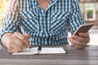 Yakın çekim iş adamı tükenmez kalem tutan ile not yazma aşağı alarak, diğer yandan açık kahve dükkanında çalışan cep akıllı telefon kullanarak. online çalışma konsepti, nesnelerin interneti.