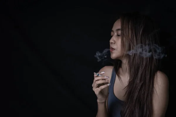 Young woman vaping, blowing cloud of smoke. Nicotine addiction toxic dangerous for healthy. Girl Smoking Cigarette on Black Background with copy space.
