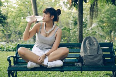 Parkta bankta oturan genç mutlu kadın. Şişe su gevşeme içki Asya backpacker kız