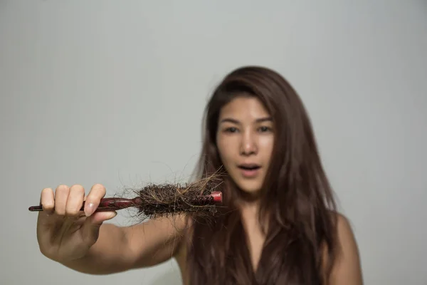 Young girl holding comb with hair fall feeling shocked.