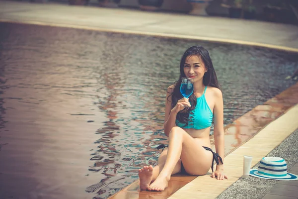 Bikini Asian girl vacation on summer at swimming pool.Sexy lady relaxing with blue cosmopolitan cocktail.Young woman enjoying tropical drinking.
