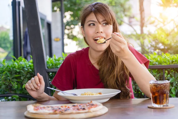 Молодая женщина ест макароны, спагетти и пиццу с безалкогольным напитком на столе в ресторане на открытом воздухе. Счастлив есть традиционную итальянскую еду, концепцию образа жизни. Голодная азиатка ест в одиночестве . — стоковое фото