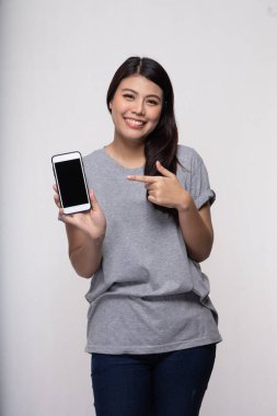 Akıllı telefonu tutan mutlu kadın beyaz arka planda boş ekranı işaret ediyor.