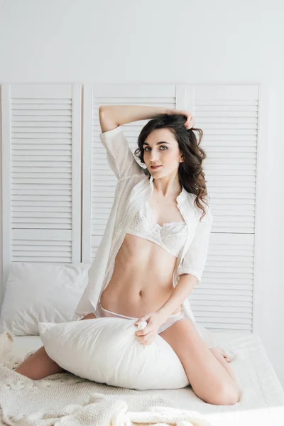 Kvinna i underkläder som sitter på sängen kramas en kudde — Stockfoto