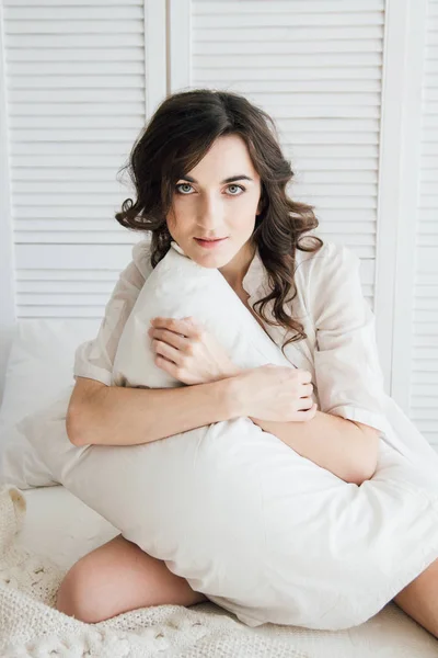 Женщина в нижнем белье сидит на кровати и обнимает подушку. — стоковое фото