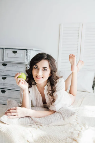 Gadis cantik berbaring di tempat tidur dan memegang Apple — Stok Foto