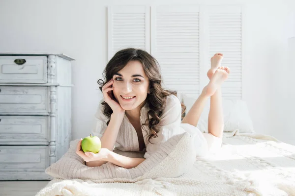Piękna dziewczyna leżąc w łóżku i trzyma jabłko — Zdjęcie stockowe