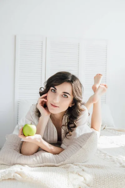 Hermosa chica acostada en la cama y sosteniendo una manzana — Foto de Stock